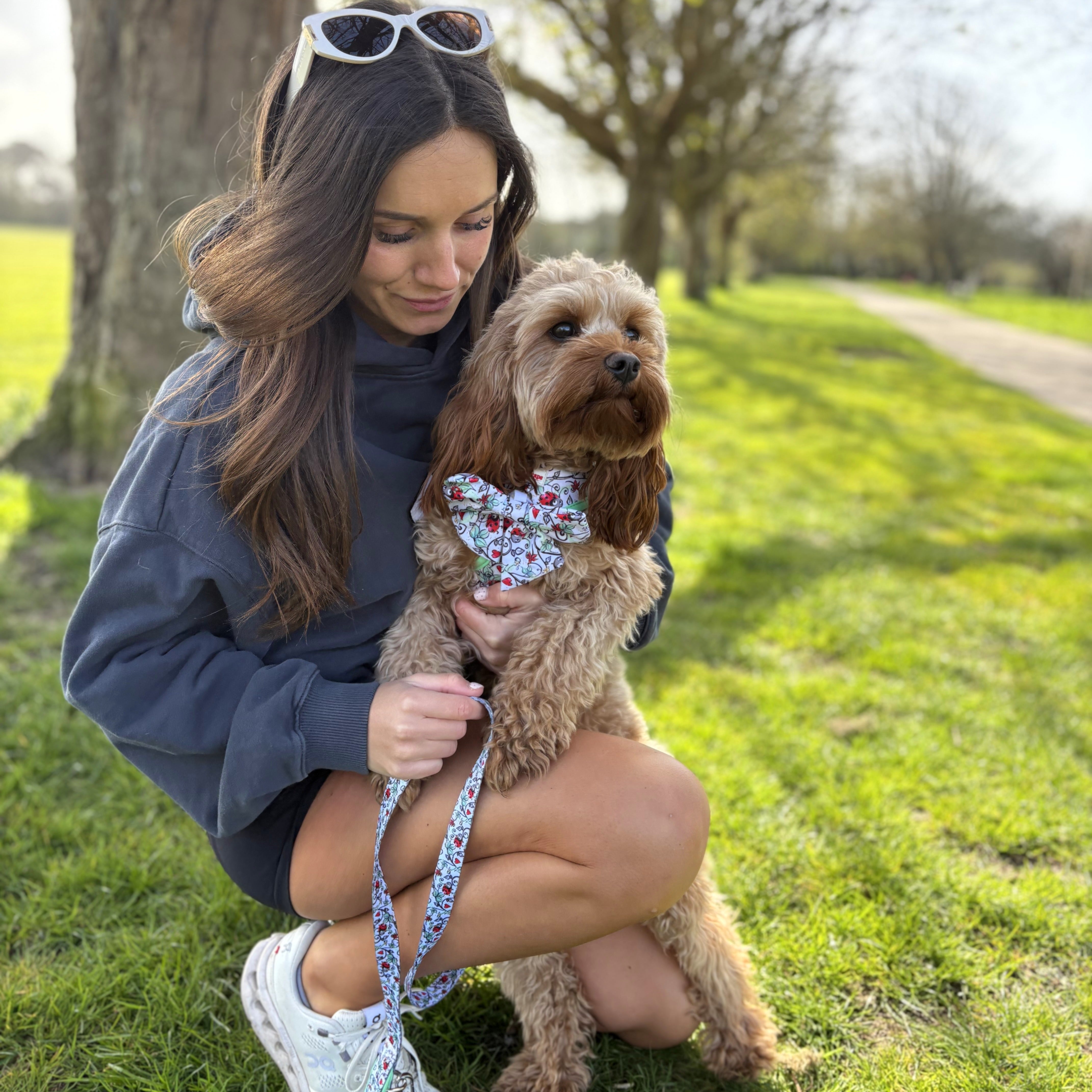 Woman holding small dog in floral bandana and matching leash outdoors