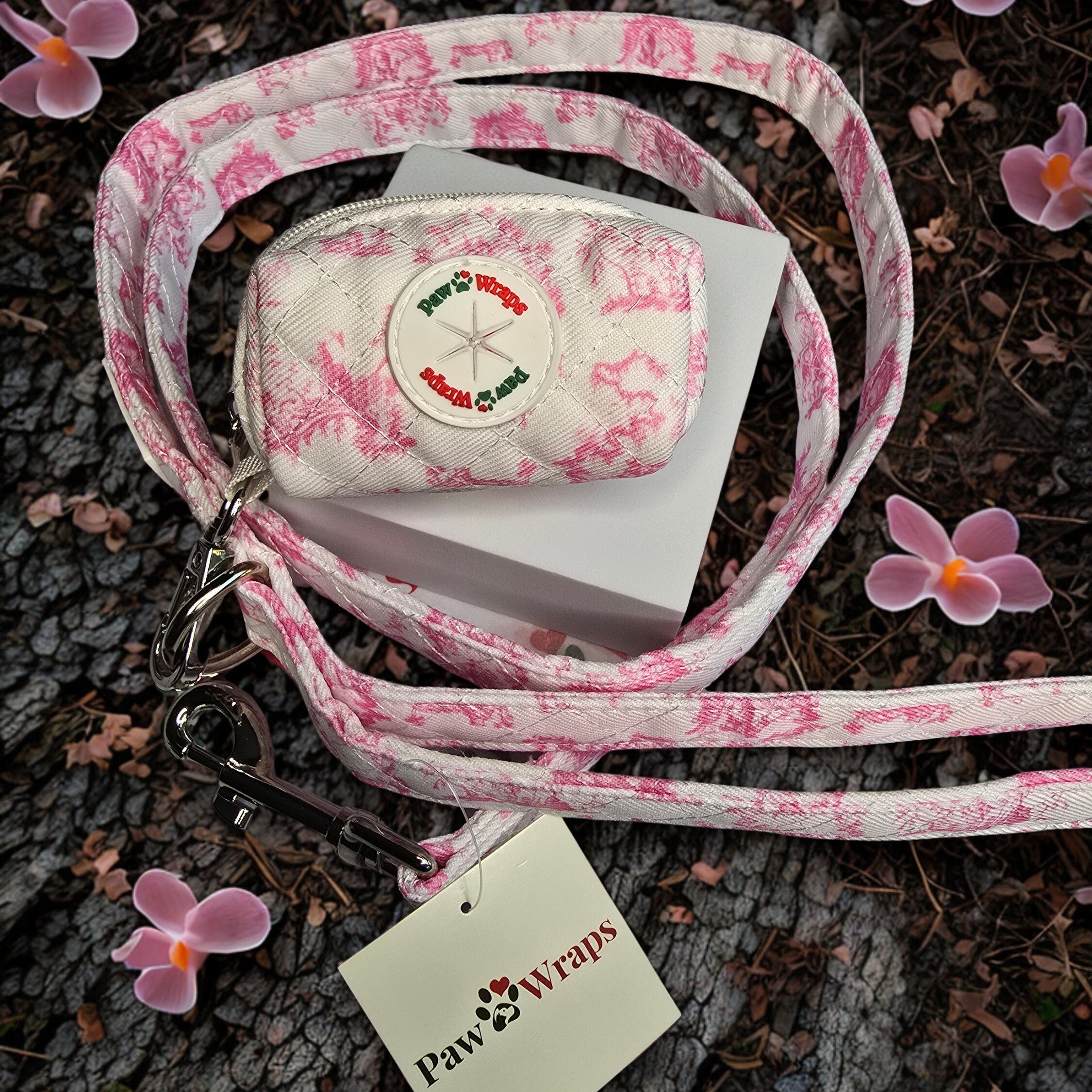 Pink floral-patterned dog leash and collar with a tag on a textured surface with flowers.