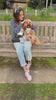 Dark haired girl sitting on a park bench with her fawn coloured cavapoo wearing a ladybirds and love hearts harness by Paw Wraps and the girl wearing a black dog walking bag crossbody by Paw wraps with Ladybird love hearts dog treats pouch attached.